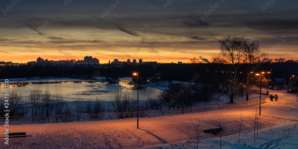 winter evening cityscape. view of the residential area across the river in the background of the sunset