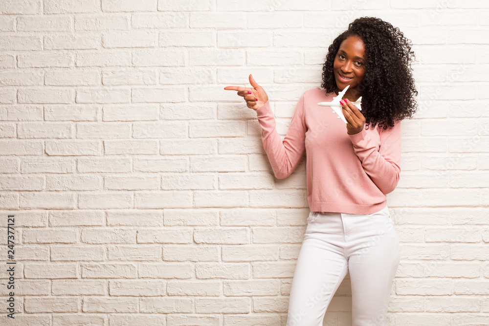 Young black woman pointing to the side, smiling surprised presenting something, natural and casual Young black woman pointing to the side, smiling surprised presenting something, natural and casual