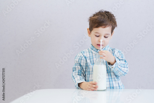 cute happy boy with dark eyes drinks milk from a bottle. the child is wearing a plaid shirt