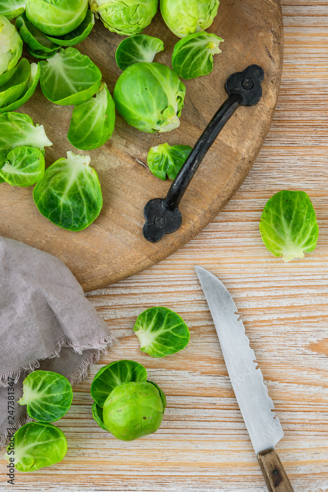 Frischer Rosenkohl auf einem auf einem Schneidebrett zusammen mit einem Messer auf einem hellen Holzuntergrund Frischer Rosenkohl auf einem auf einem Schneidebrett zusammen mit einem Messer auf einem hellen Holzuntergrund