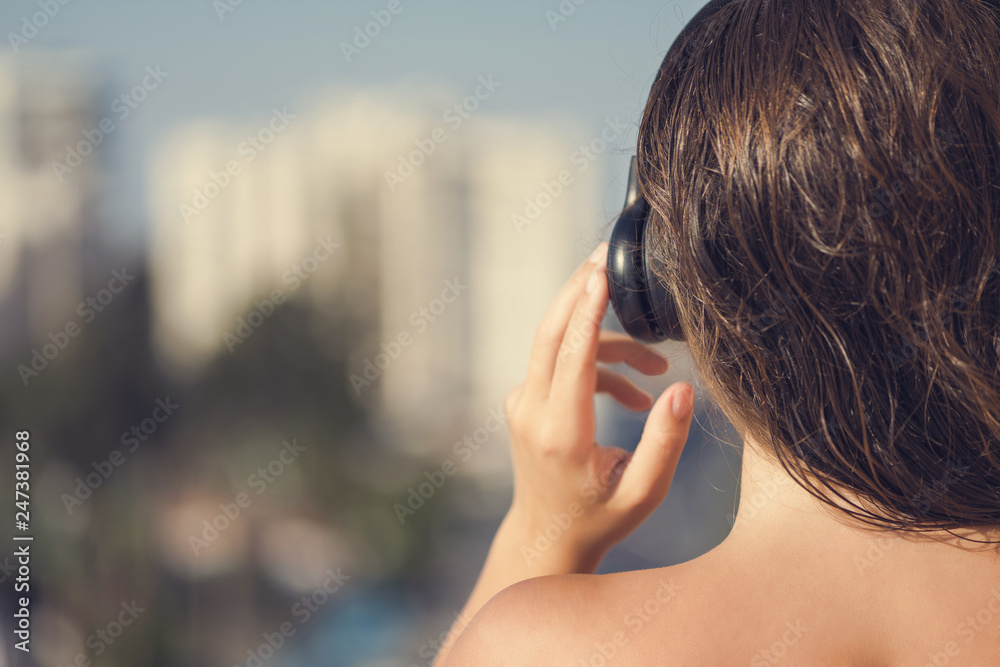 Naked beautiful woman with wet hair in a headphones on the balcony of her apartment against the backdrop of the resort town and the sea.