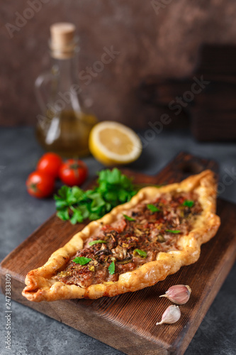 Turkish handmade pide lies on an blue surface. Cherry tomatoes, parsley, lemon, hot pepper, garlic are on the table.