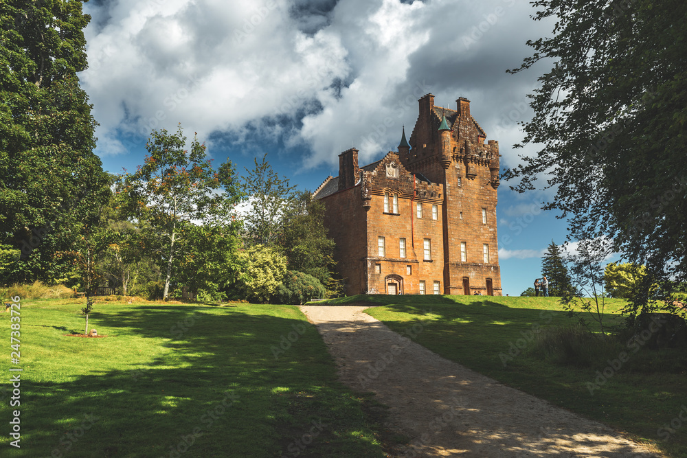 Obraz premium Path to the ancient castle. Northern Ireland. Picturesque scene the vintage building surrounded by the green lawn and trees. Blue cloudy sky background. Stunning Irish landscape. Historical house.