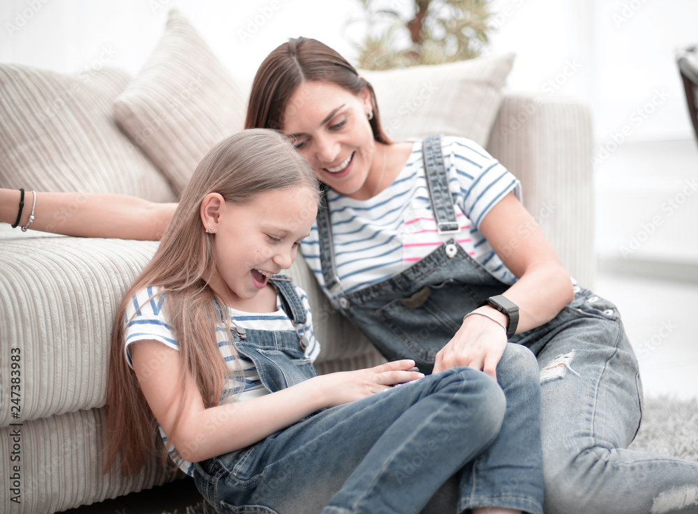 Mother with a little daughter using a smartphone sitting in the new living room Mother with a little daughter using a smartphone sitting in the new living room