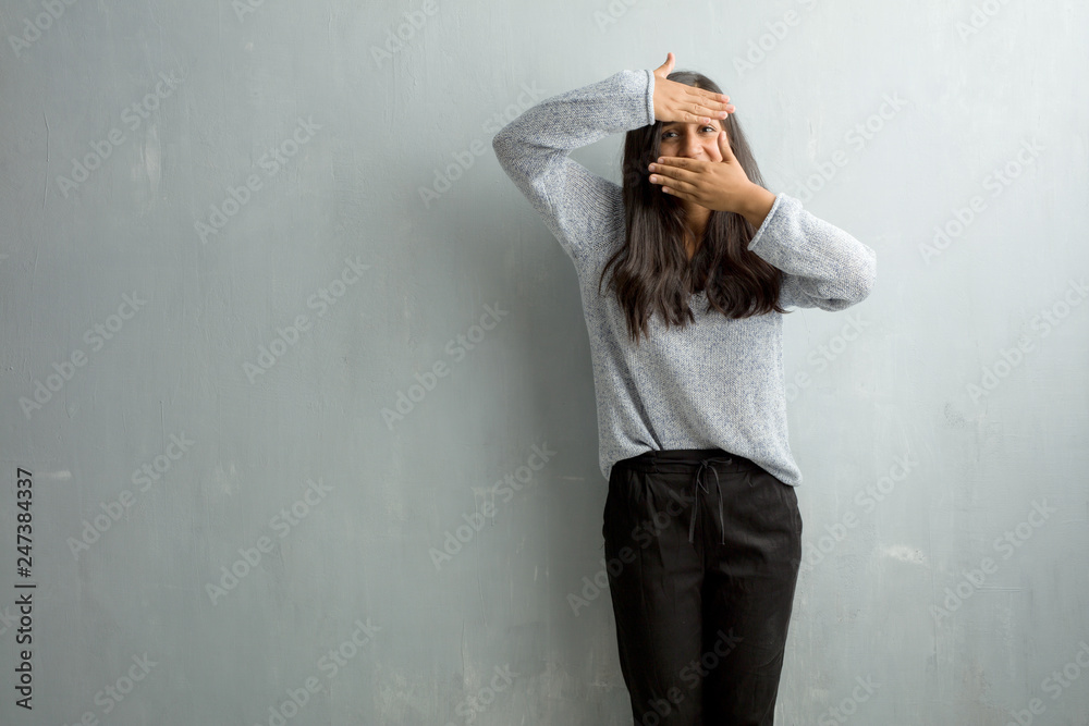 Young indian woman against a grunge wall looking through a gap, hiding and squinting Young indian woman against a grunge wall looking through a gap, hiding and squinting