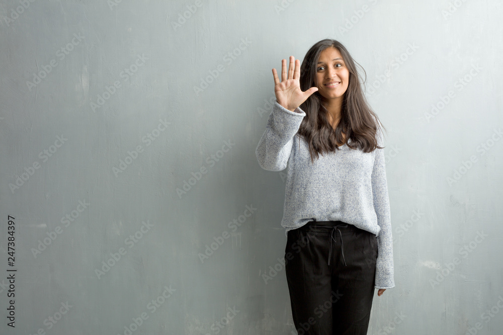 Young indian woman against a grunge wall showing number five, symbol of counting, concept of mathematics, confident and cheerful Young indian woman against a grunge wall showing number five, symbol of counting, concept of mathematics, confident and cheerful