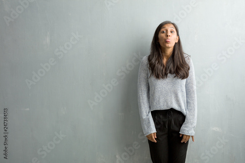 Young indian woman against a grunge wall expression of confidence and emotion, fun and friendly, showing tongue as a sign of play or fun