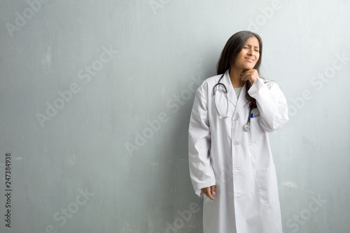 Young indian doctor woman against a wall with a sore throat, sick due to a virus, tired and overwhelmed