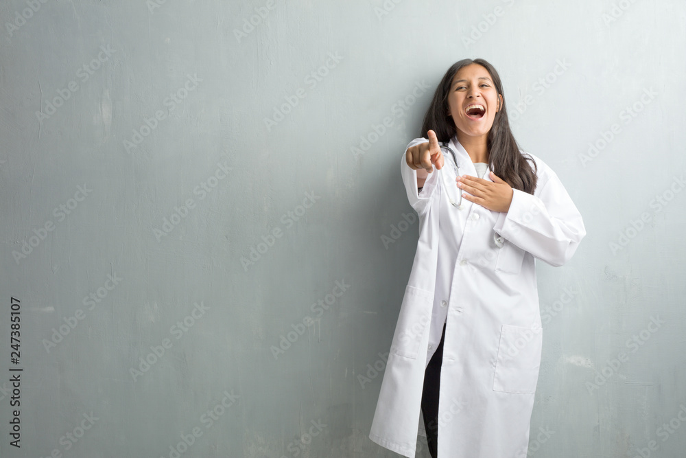 Young indian doctor woman against a wall shouting, laughing and making fun of another, concept of mockery and uncontrol Young indian doctor woman against a wall shouting, laughing and making fun of another, concept of mockery and uncontrol