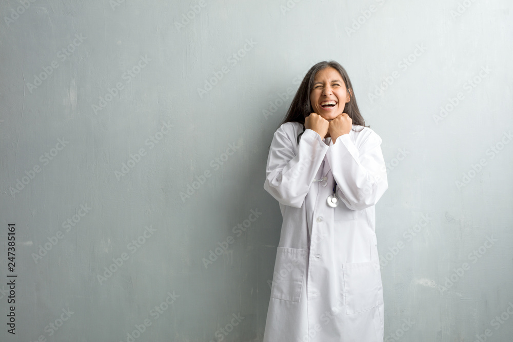 Young indian doctor woman against a wall very happy and excited, raising arms, celebrating a victory or success, winning the lottery Young indian doctor woman against a wall very happy and excited, raising arms, celebrating a victory or success, winning the lottery