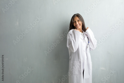 Young indian doctor woman against a wall very happy and excited, raising arms, celebrating a victory or success, winning the lottery