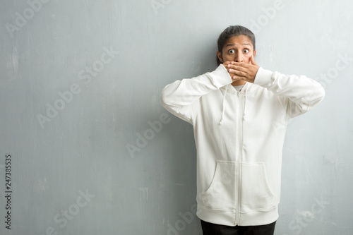 Young sporty indian woman against a gym wall covering mouth, symbol of silence and repression, trying not to say anything