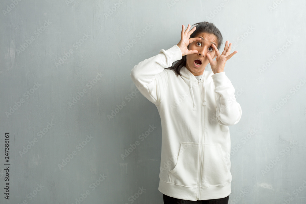 Young sporty indian woman against a gym wall surprised and shocked, looking with wide eyes, excited by an offer or by a new job, win concept Young sporty indian woman against a gym wall surprised and shocked, looking with wide eyes, excited by an offer or by a new job, win concept