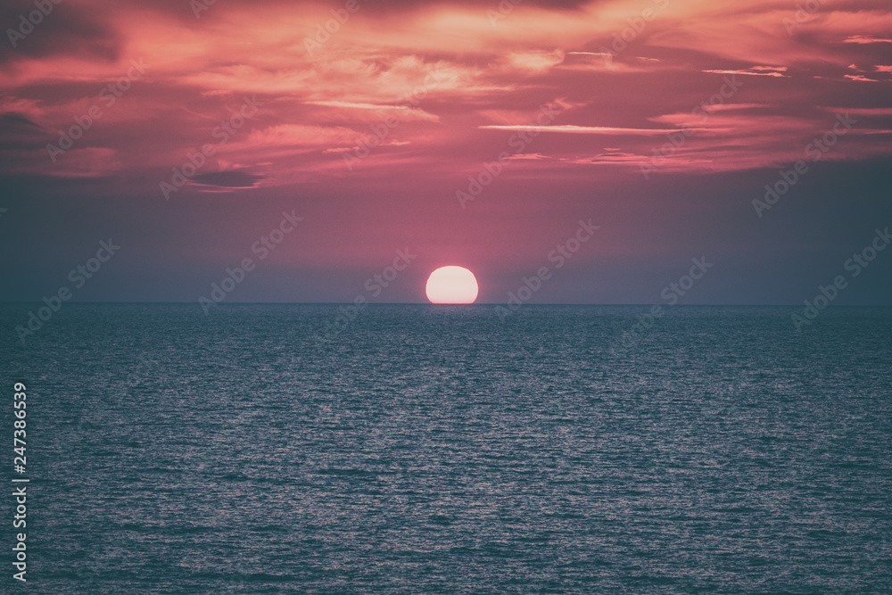 Scenic sunset seascape with sea, sun and amazing scarlet cloudy sky, outdoor travel vintage background