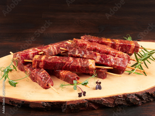 Raw fresh beef and lamb skewers, uncooked, on a wood board, garnished with fresh pea shoots and rosemary sprigs