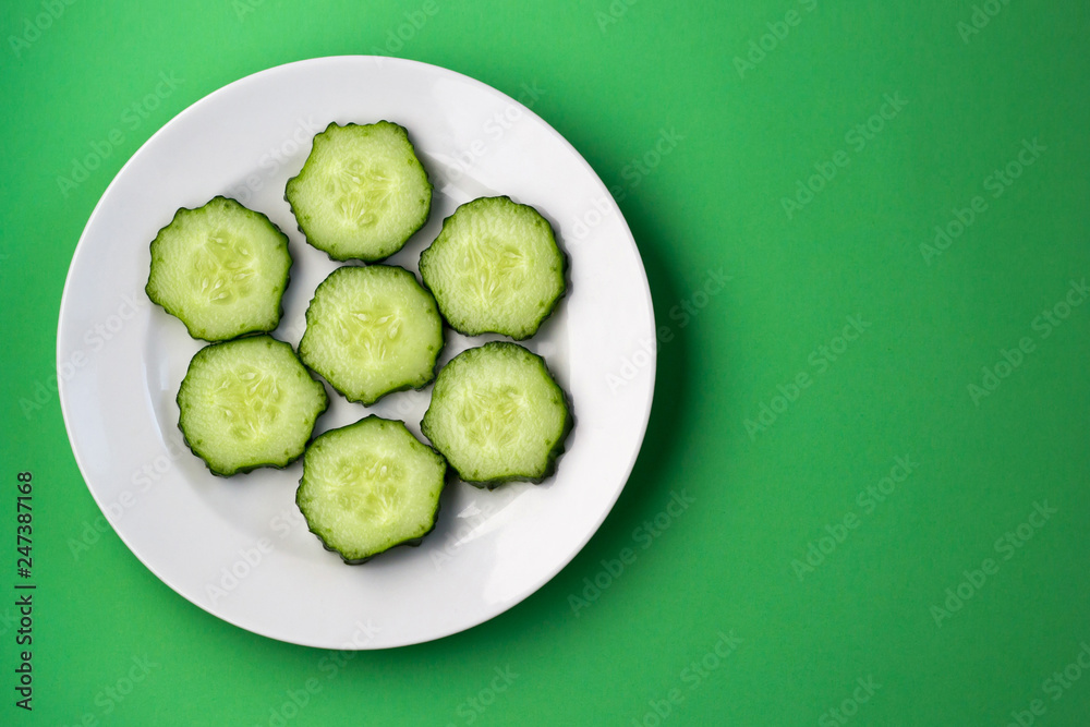 Top view of a plate with sliced cucumber slices on a green background. Top view of a plate with sliced cucumber slices on a green background.