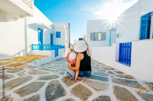 Mum and daughter in white hats sit hugging and taking great selfie on the beatiful sunshine greek street photo