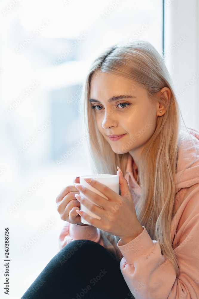 An elf alike, young girl enjoying a cup of coffee or milk while sitting by the window indoors An elf alike, young girl enjoying a cup of coffee or milk while sitting by the window indoors