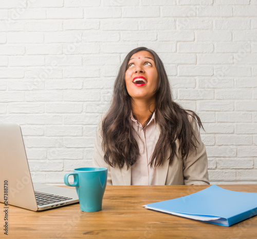 Young indian woman at the office looking up, thinking of something fun and having an idea, concept of imagination, happy and excited