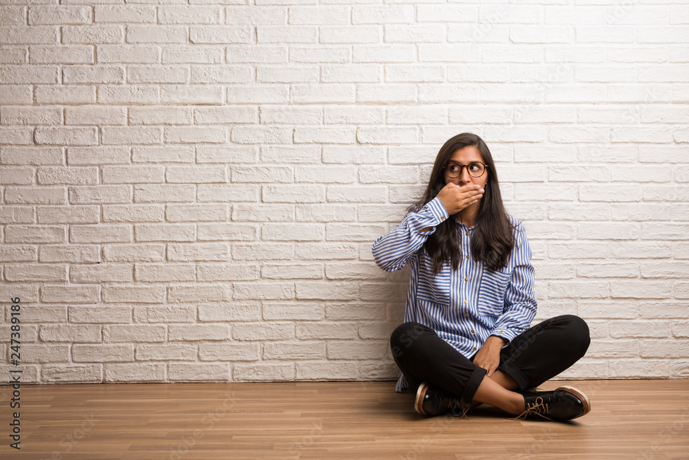 Young indian woman sit against a brick wall covering mouth, symbol of silence and repression, trying not to say anything Young indian woman sit against a brick wall covering mouth, symbol of silence and repression, trying not to say anything