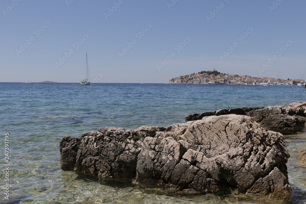 Sailboats, yachts on the Adriatic Sea. Beautiful weather. Sunny, hot, summer day on the Croatian coast. Town ​​Primosten in the background. Rocky shore, mediterranean, riviera, seashore, Croatia