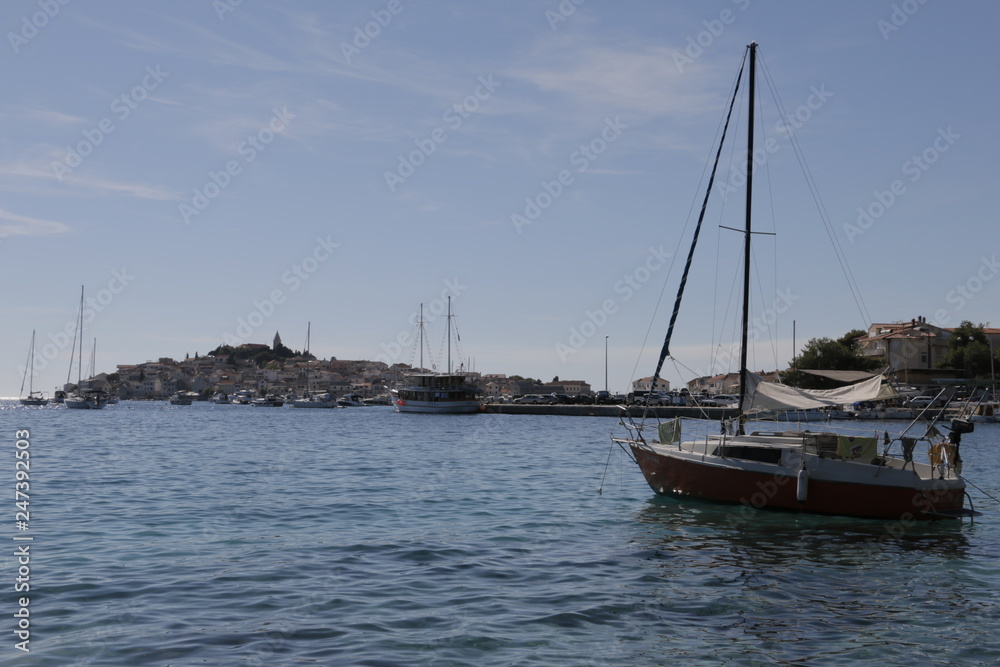 Sailboats, yachts on the Adriatic Sea. Beautiful weather. Sunny, hot, summer day on the Croatian coast. ​​Primosten in the background. Rocky shore, mediterranean vegetation, seashore, Croatia