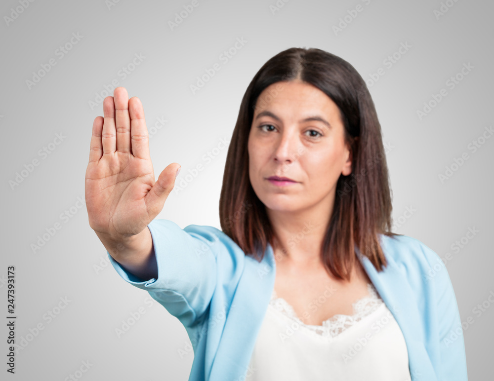 Middle aged woman serious and determined, putting hand in front, stop gesture, deny concept