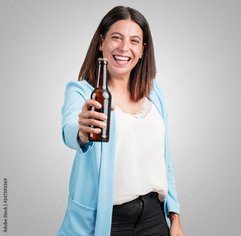 Middle aged woman happy and fun, holding a bottle of beer, feels good after an intense day of work, ready to watch a soccer match on television Middle aged woman happy and fun, holding a bottle of beer, feels good after an intense day of work, ready to watch a soccer match on television