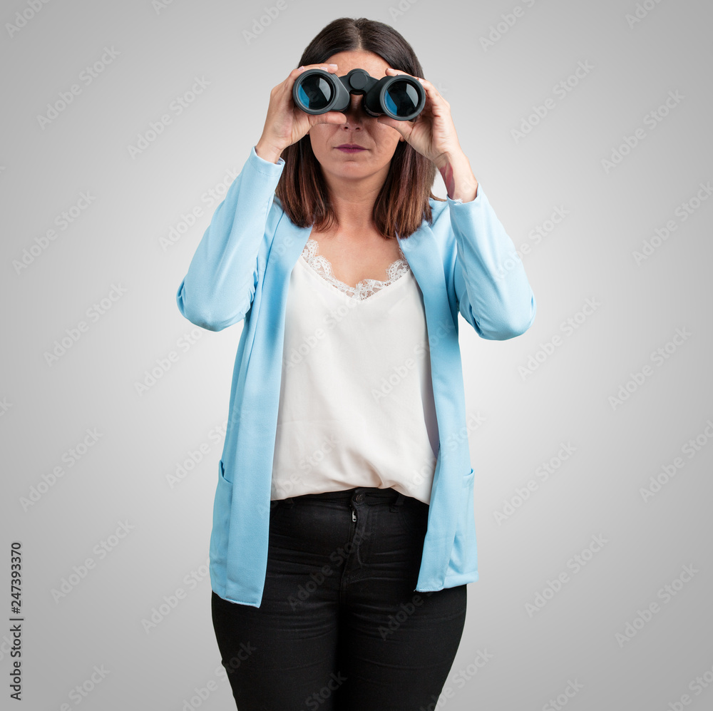 Middle aged woman surprised and amazed, looking with binoculars in the distance something interesting, concept of future opportunity Middle aged woman surprised and amazed, looking with binoculars in the distance something interesting, concept of future opportunity