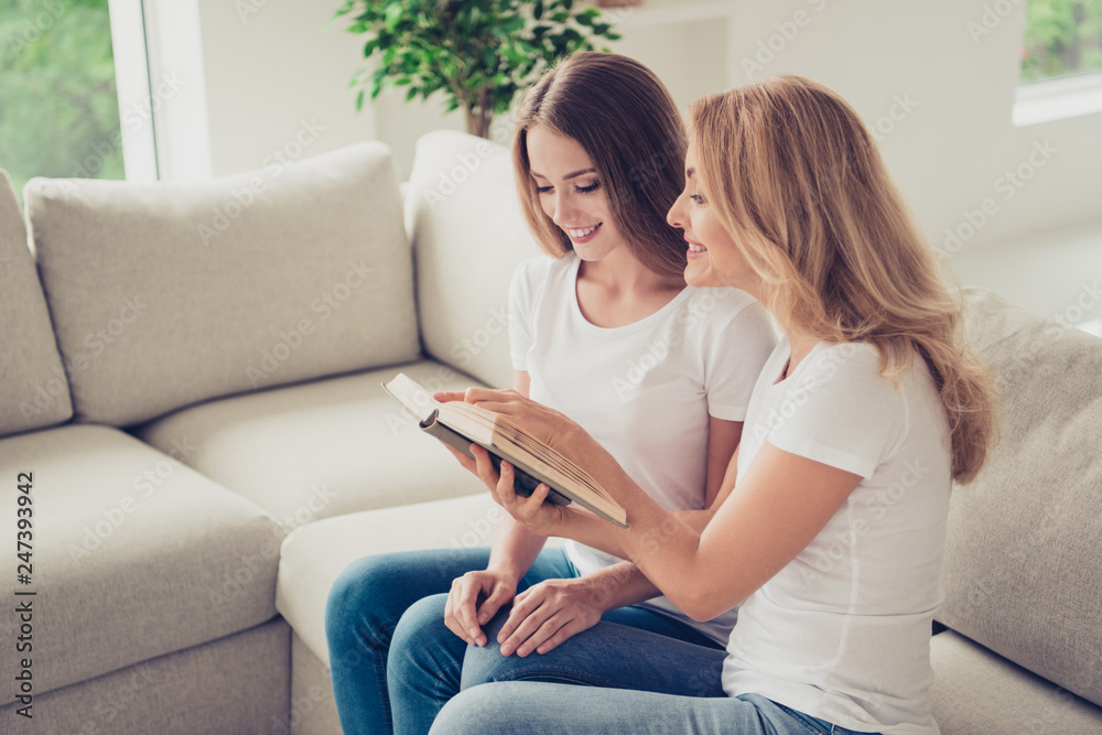 Close up photo of two people mum and teen daughter lovely look to open book holding hands arms adventure novel showing favorite moment wear white t-shirts jeans sit on comfy sofa Close up photo of two people mum and teen daughter lovely look to open book holding hands arms adventure novel showing favorite moment wear white t-shirts jeans sit on comfy sofa