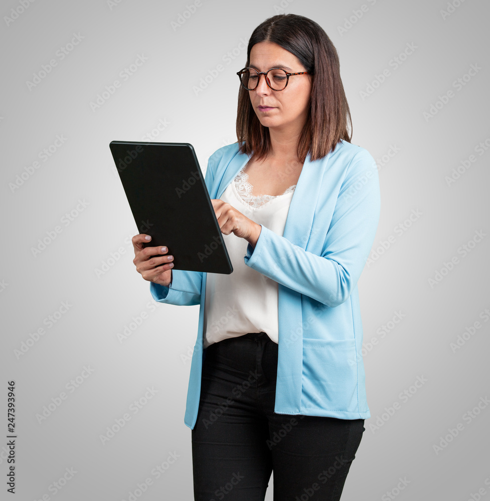 Middle aged woman smiling and confident, holding a tablet, using it to surf the internet and see social networks, communication concept Middle aged woman smiling and confident, holding a tablet, using it to surf the internet and see social networks, communication concept