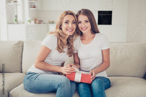 Close up photo two people mum and teen daughter holding hands arms unexpected gift box surprise satisfied wear white t-shirts jeans in bright kitchen sit on cozy comfy comfortable sofa