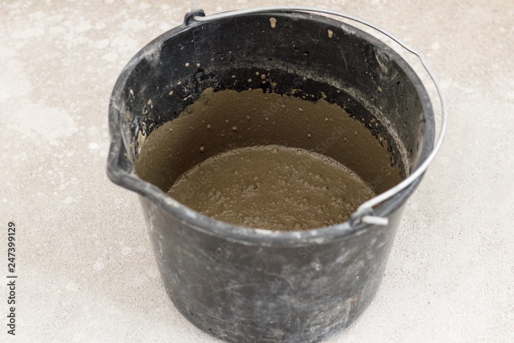 dark bucket. This is the solution for leveling the floor. on the background of the biton floor, and poured out of it dark bucket. This is the solution for leveling the floor. on the background of the biton floor, and poured out of it
