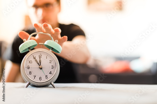 Man is pushing an alarm clock in the morning, sunshine and blurry background
