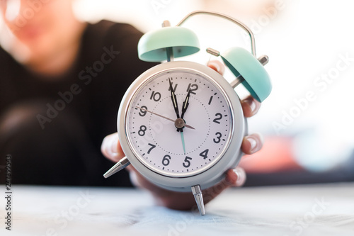 Man is holding an alarm clock in the hand, blurry background