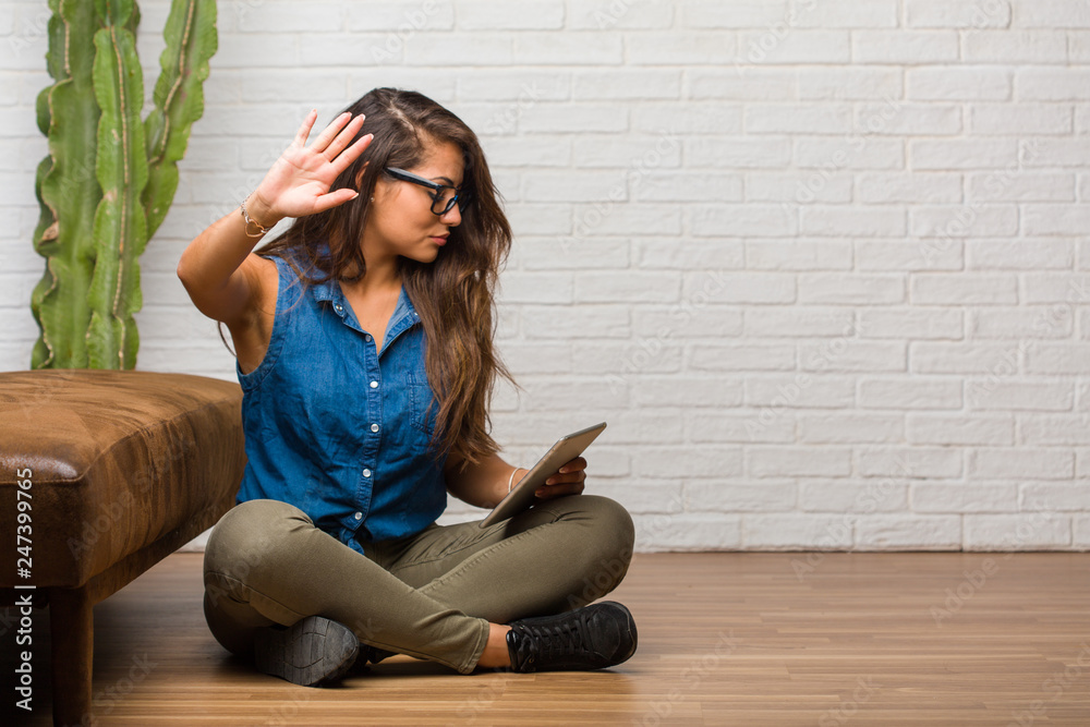 Portrait of young latin woman sitting on the floor serious and determined, putting hand in front, stop gesture, deny concept. Holding a tablet. Portrait of young latin woman sitting on the floor serious and determined, putting hand in front, stop gesture, deny concept. Holding a tablet.