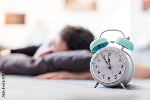 Alarm clock in the morning. Young man sleeps in the blurry background.