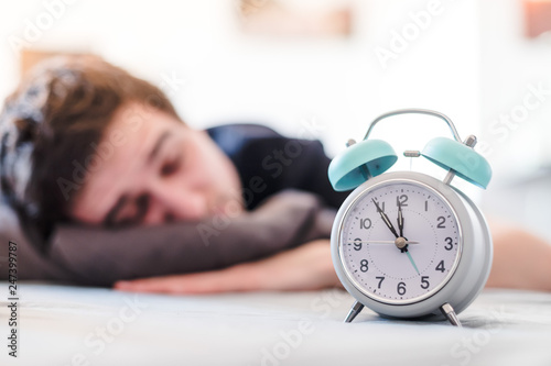 Alarm clock in the morning. Young man sleeps in the blurry background.