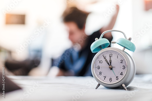 Alarm clock in the morning. Young wakes up and stretches in the blurry background.