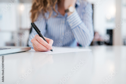 Low angle image of businesswoman in formal wear writing with pen on paper, close-up, copy space.