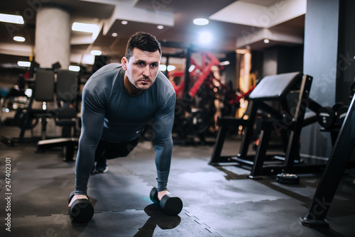 Strong and handsome man doing plank exercise on dummbells, front view. photo