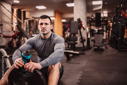 Portrait of a handsome bodybuilder sitting on the floor in the gym, looking at camera.