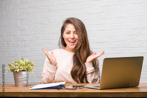 Portrait of young student latin woman sitting on her desk surprised and shocked, looking with wide eyes, excited by an offer or by a new job, win concept