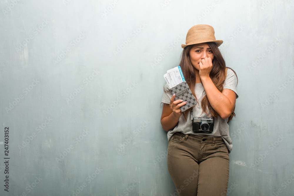 Portrait of young traveler latin woman against a wall biting nails, nervous and very anxious and scared for the future, feels panic and stress. Holding her passport and boarding pass. Portrait of young traveler latin woman against a wall biting nails, nervous and very anxious and scared for the future, feels panic and stress. Holding her passport and boarding pass.