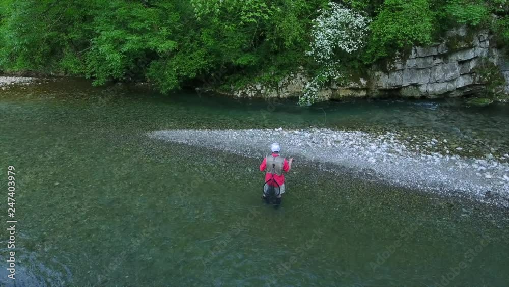 aerial picture fisherman in rubber boots stands in shallow mountain river throws rod near rocky islet at forestry bank aerial picture fisherman in rubber boots stands in shallow mountain river throws rod near rocky islet at forestry bank