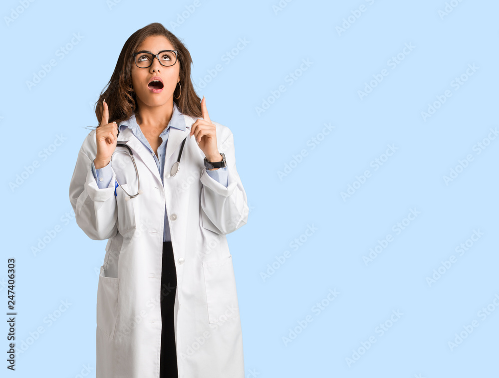 Full body young doctor woman surprised pointing up to show something Full body young doctor woman surprised pointing up to show something