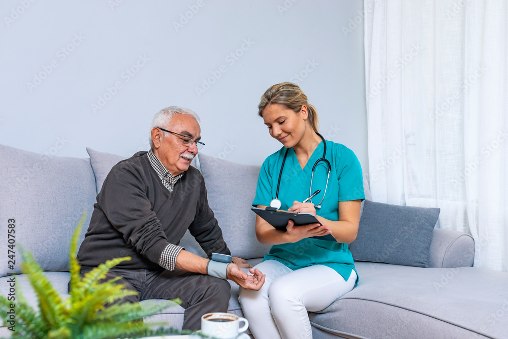 Nurse Visiting Senior man For Check Up. Young nurse measuring blood pressure of elderly man at home. Happy senior man having her blood pressure measured in a nursing home by her caregiver - obrazy, fototapety, plakaty 