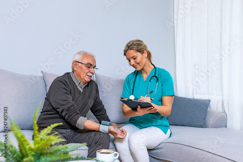 Nurse Visiting Senior man For Check Up. Young nurse measuring blood pressure of elderly man at home. Happy senior man having her blood pressure measured in a nursing home by her caregiver