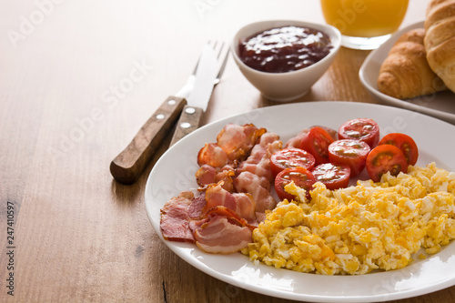 Breakfast with scrambled eggs, bacon, tomatoes,coffee,orange juice ,croissant and corn flakes on wooden table