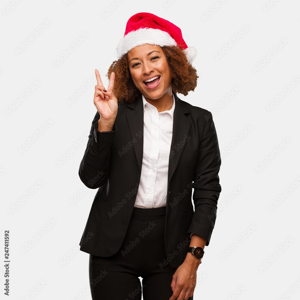 Young business black woman wearing a chirstmas santa hat fun and happy doing a gesture of victory Young business black woman wearing a chirstmas santa hat fun and happy doing a gesture of victory